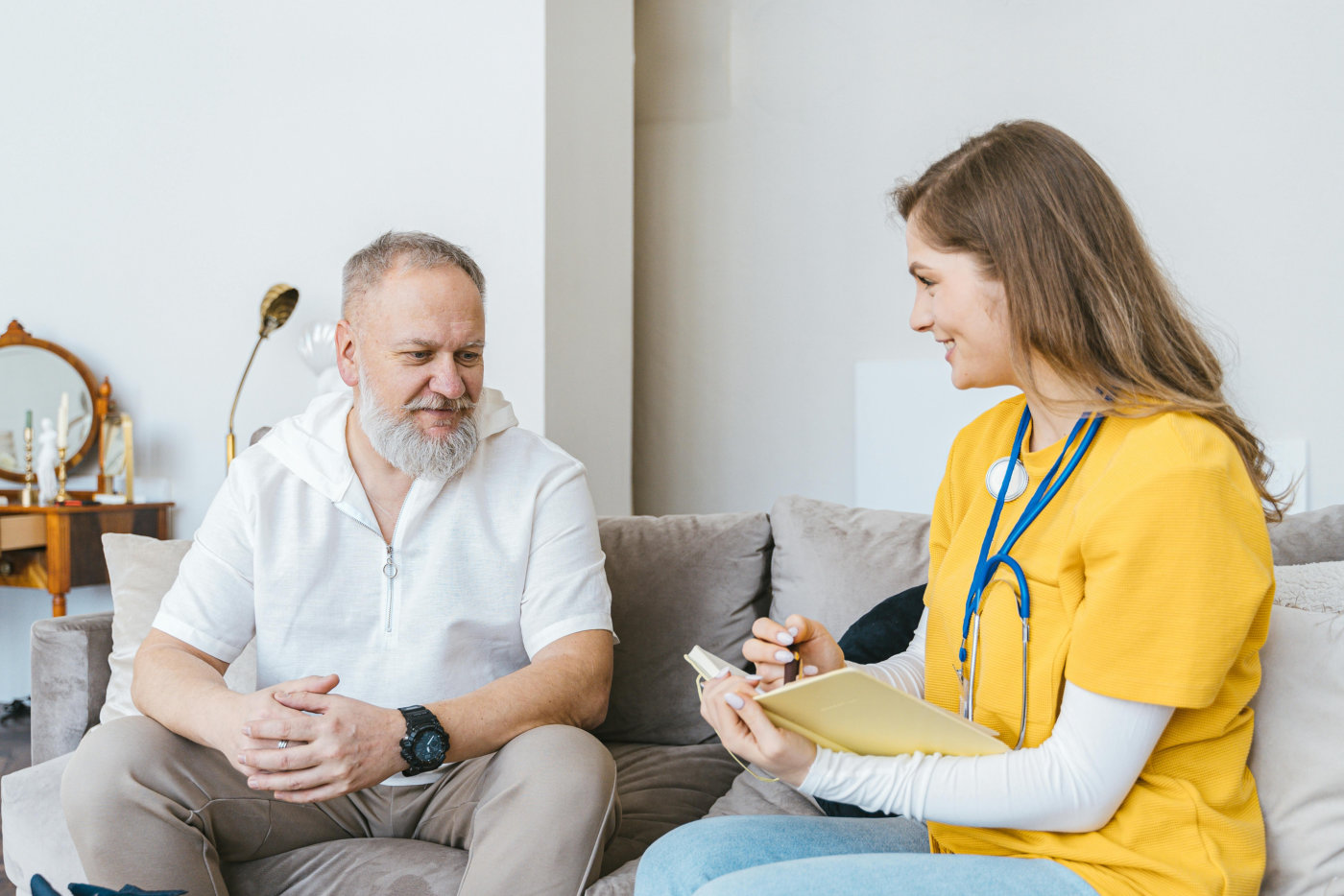 A senior and caregiver are seated on a couch, engaged in a lively discussion.