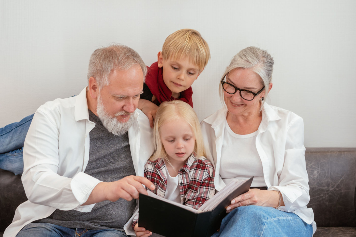 Grandparents and grandchildren reading a photo album on the couch, embracing family bonds and love