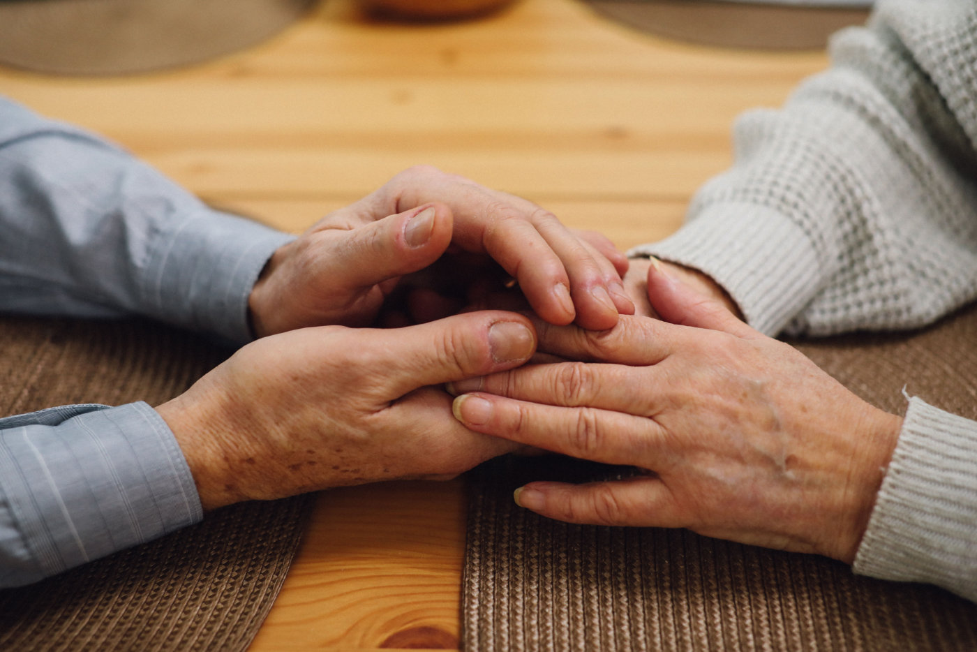 Two elderly individuals holding hands across a table, symbolizing companionship and affection.
